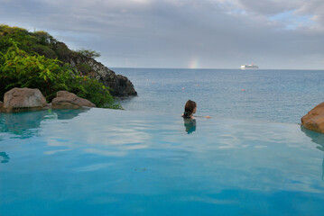 Young teenage girl looking at the ocean from an infiinity pool