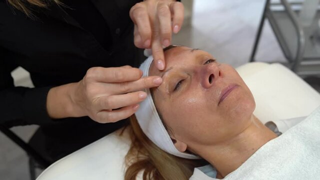 Beautiful happy caucasian woman  doing face massage to client at spa - Female beautician doctor cosmetologist applying face mask at salon - healthcare concept