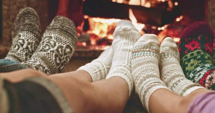 Feet in woolen socks warming by cozy fire in Christmas time in slow motion. Family with two kids warming their feet by the fireplace in winter time. Filmed at 120 fps 4k graded from RAW
