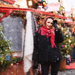 Outdoors lifestyle fashion portrait of stunning blonde young woman. Smiling, walking on the christmas market. Going shopping. Trendsetter. Wearing stylish black fur coat and scarf. Festive mood