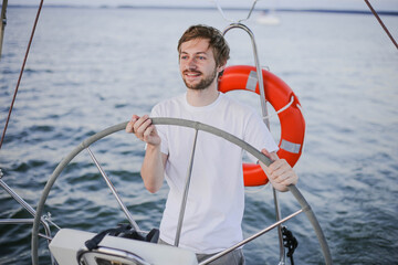 Happy young man steering wheel and looking far away on yacht on the sea. Sailing