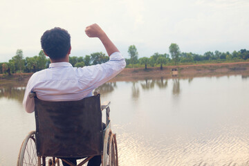 Young disabled man with river background.He is sitting on wheelchair and looking into...