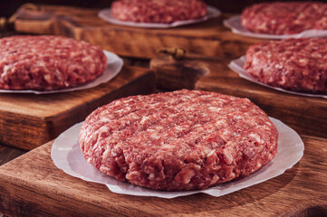 Raw hamburgers on cutting board with wood pile background - Close-up
