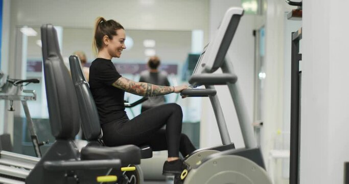 woman exercising with elliptical cross trainer at gym.Side view, slow motion. Woman training at elliptical bike. Woman pedaling at gym