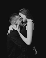 Man and woman kissing each other on a black background. The girl bites the guy on the nose. Black background Guy and girl holding hands. Couple hugging. Love.