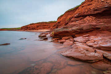 Fototapeta na wymiar At Cavendish beach, on Canada's Prince Edward Island, the flat red sandstone has been weathered by winds and ocean currents. The red cliff overlooks the Atlantic ocean with a rolling hillside.