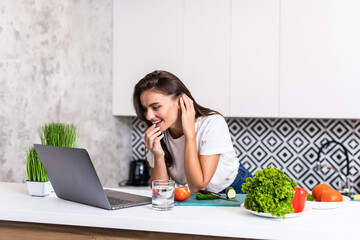Beautiful young woman cooking with receipt on laptop in the kitchen