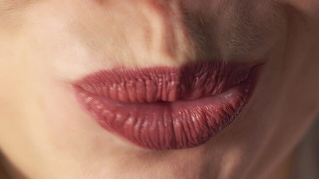 Close up of smiling and gesturing female mouth with healthy white teeth and matte lipstick. There is a macro of young caucasian woman's lips. She grimaces. Concept of stomatology or cosmetic medicine.