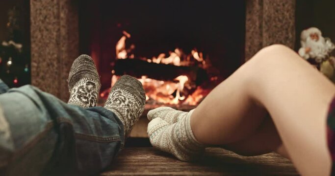 Feet in woolen socks warming by cozy fire in Christmas time in slow motion. Family couple warming their feet by the fireplace in winter time. Filmed at 120 fps 4k graded from RAW