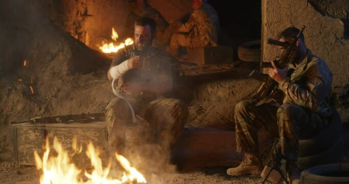 Soldiers tending wounds and checking rifle near campfire