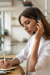 Focused woman consultant in shirt wear headphones communicating with clients, talking on video...