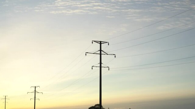 High voltage line on the background of dawn. Yellow sunrise light on the sky. Countryside plain with a view of the electrical power poles silhouettes in perspective. Industrial panorama.