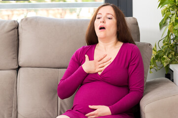 Shot of a pregnant woman suffering respiration problems sitting on a couch in the living room at...