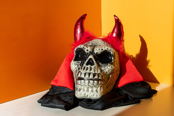 Skull in devil costume with horns an orange background, illuminated by sunlight.
