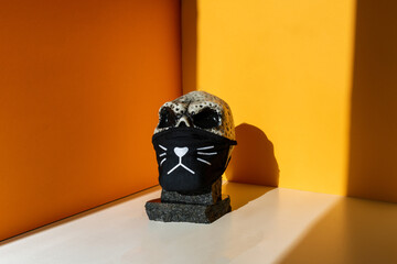 New normal concept. Skull in a protective medical mask on an orange background, illuminated by...