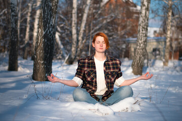 Beautiful young woman sits in yoga position in frozen mountain forest. Cute girl meditates in winter park.