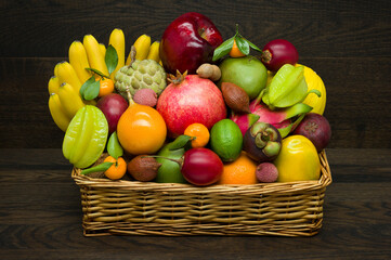 Exotic tropical fruits in wicker basket on wooden background, healthy food, diet nutrition 
