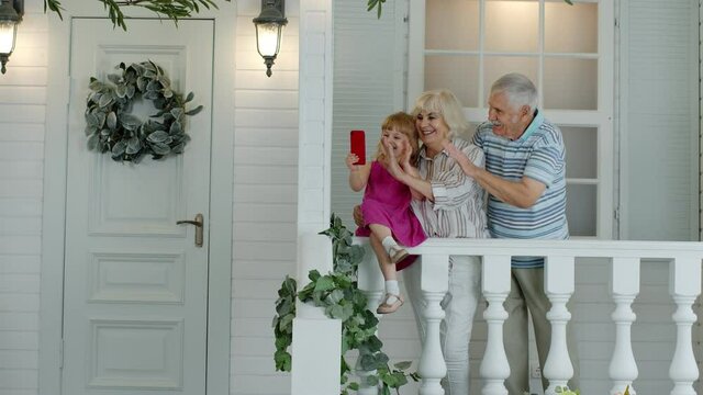 Senior ouple sitting with granddaughter in porch at home. Using mobile phone for online video call