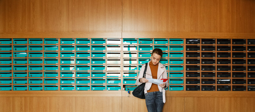 Young woman reading mail leaning on mailboxes in long rows