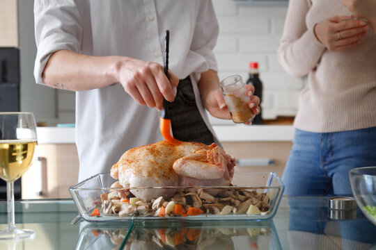 Woman greasing seasoned poultry in dish at table in kitchen