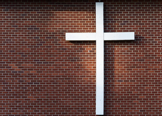 Simple white wooden cross on an exterior red brick wall, sunbeam on the wall
