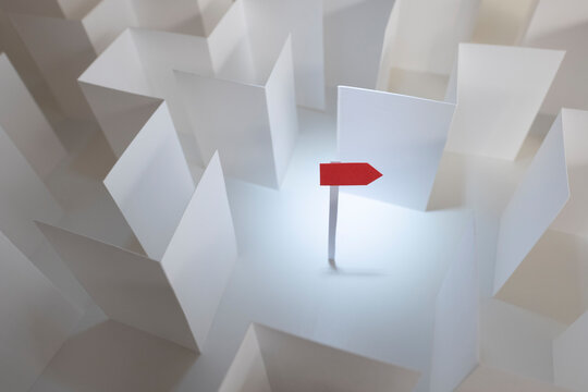 Finding our way out, a red paper sign points the way out of a white paper maze,