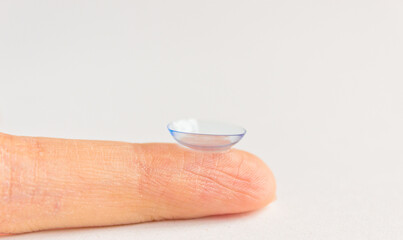 Contact lens on human finger on grey background. Selective focus. Close up