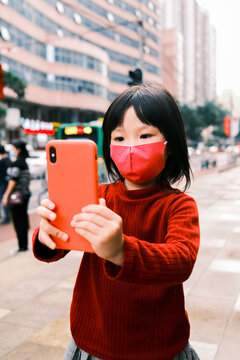 Little girl wearing a mask and using cell phone in street