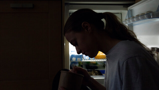 Woman eating near fridge at night