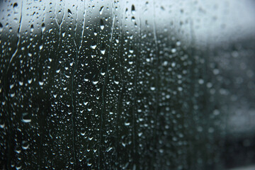 Selective focus of rain drops on window glasses surface with cloudy background. Dramatic background concept
