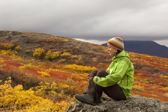 Young woman sitting on a rock, resting, enjoying view, subalpine tundra, Indian summer, autumn, near Fish Lake, Yukon Territory, Canada, North America