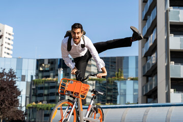 Carefree businessman performing stunt on electric bicycle against clear sky in city