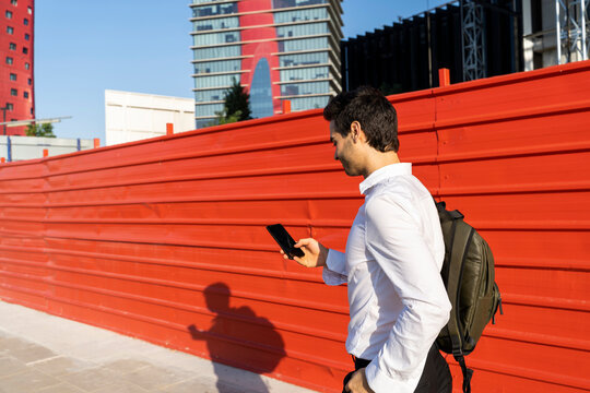 Male entrepreneur using mobile phone while walking by wall in city