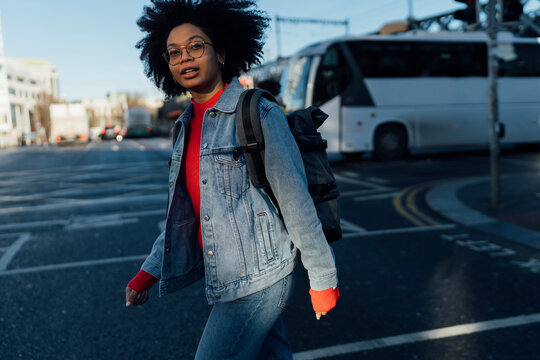 Afro young woman wearing denim jacket crossing road in city
