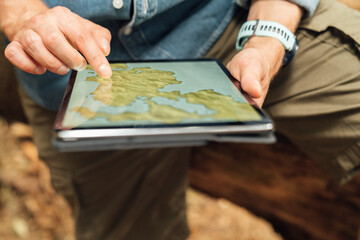 Close-up of man's hands using map over digital tablet in forest