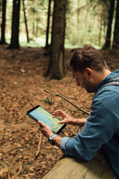Male hiker analyzing map on digital tablet while standing in forest