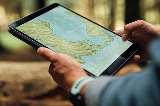 Close-up of mid adult man's hands analyzing map over digital tablet in forest