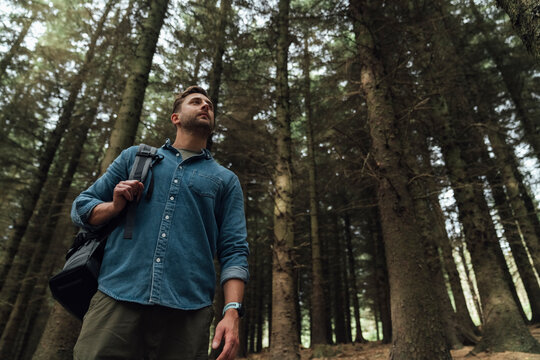 Mid adult man contemplating while standing against trees in forest
