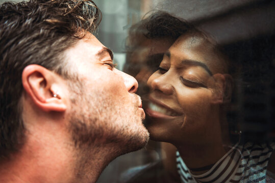 Close-up of romantic man kissing girlfriend through glass window