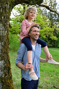 Smiling father carrying daughter on shoulder while exploring forest