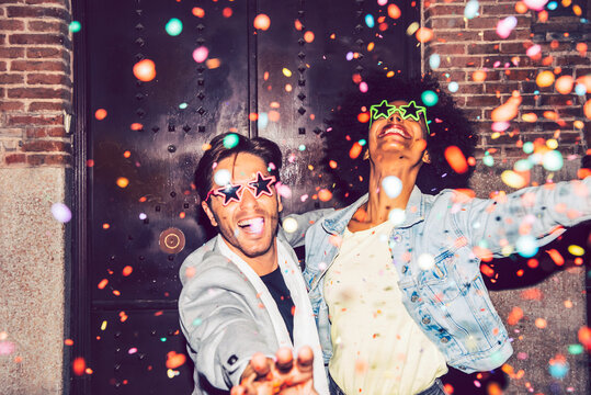 Confetti falling on cheerful couple wearing star shaped sunglasses enjoying outdoors at night