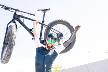 Cheerful male amputee athlete carrying bicycle while standing against clear sky