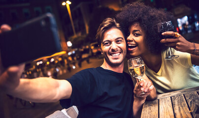 Cheerful couple holding wineglasses taking selfie at date night
