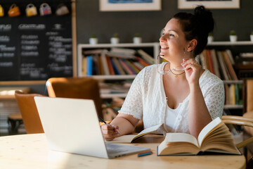 Voluptuous woman with books and laptop on table contemplating while sitting in cafe