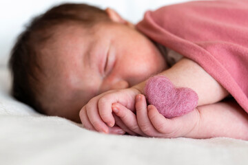 Close-up of newborn baby girl with heart shape sleeping on bed in hospital
