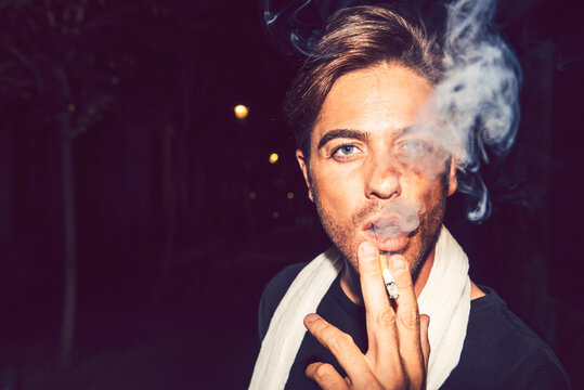 Close-up of handsome man smoking cigarette outdoors at night
