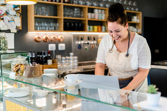 Cheerful female owner using laptop while standing in coffee shop