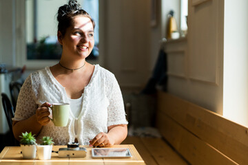 Young woman holding coffee mug contemplating while sitting at table in cafe