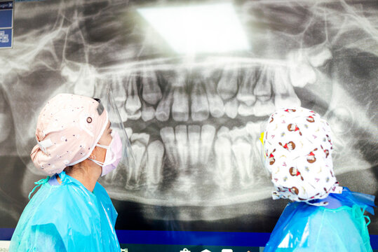 Dentist and assistant in protective workwear examining dental x-ray at office