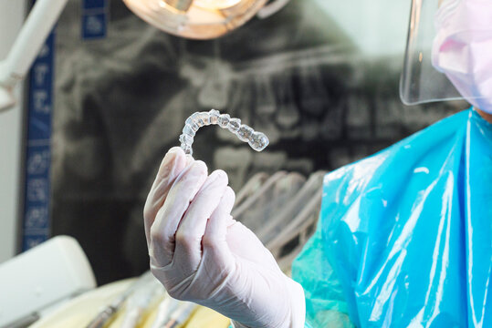 Dentist wearing protective suit holding dental aligner in hand at clinic